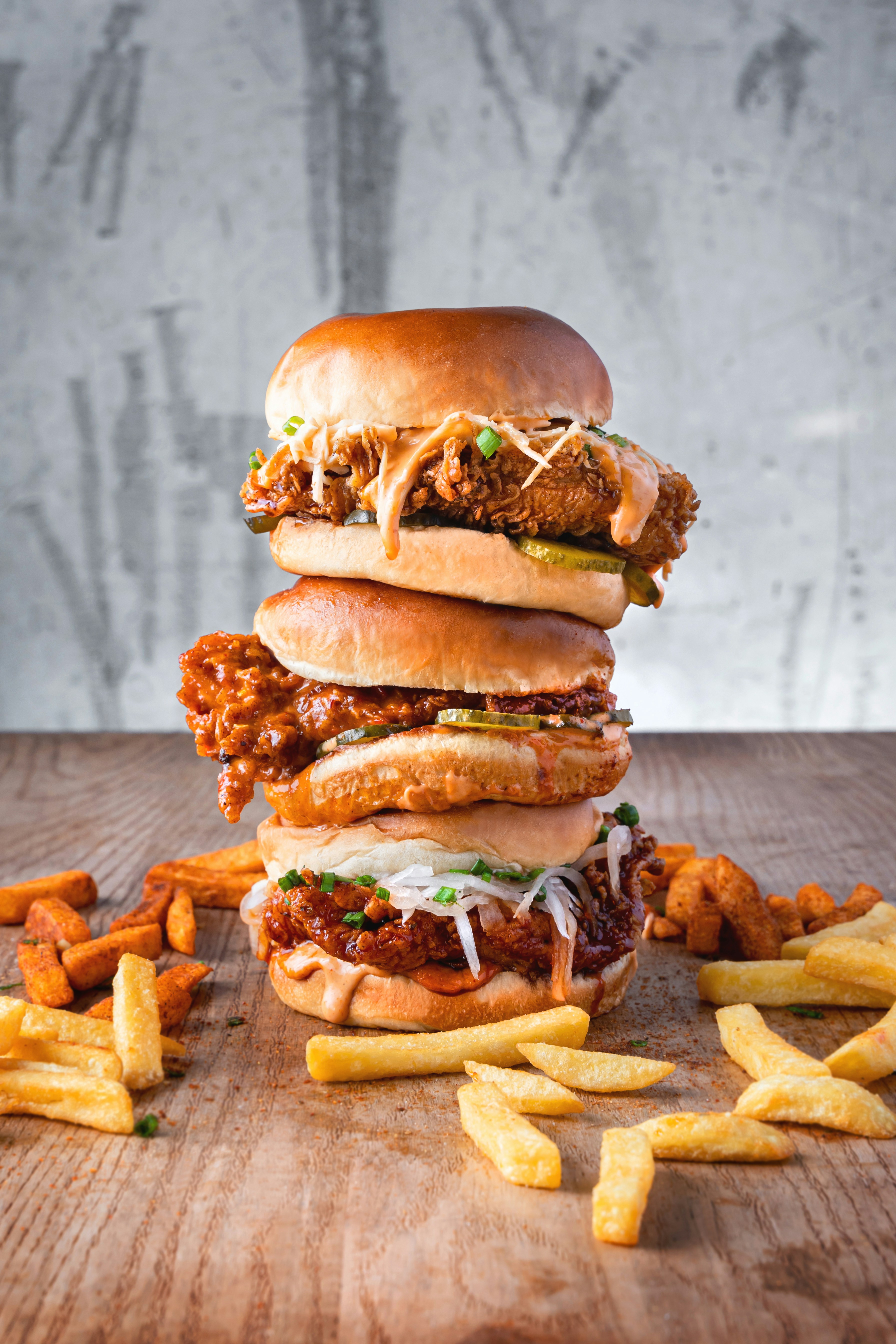 Three sandwiches stacked on top of each other with fries on the ground